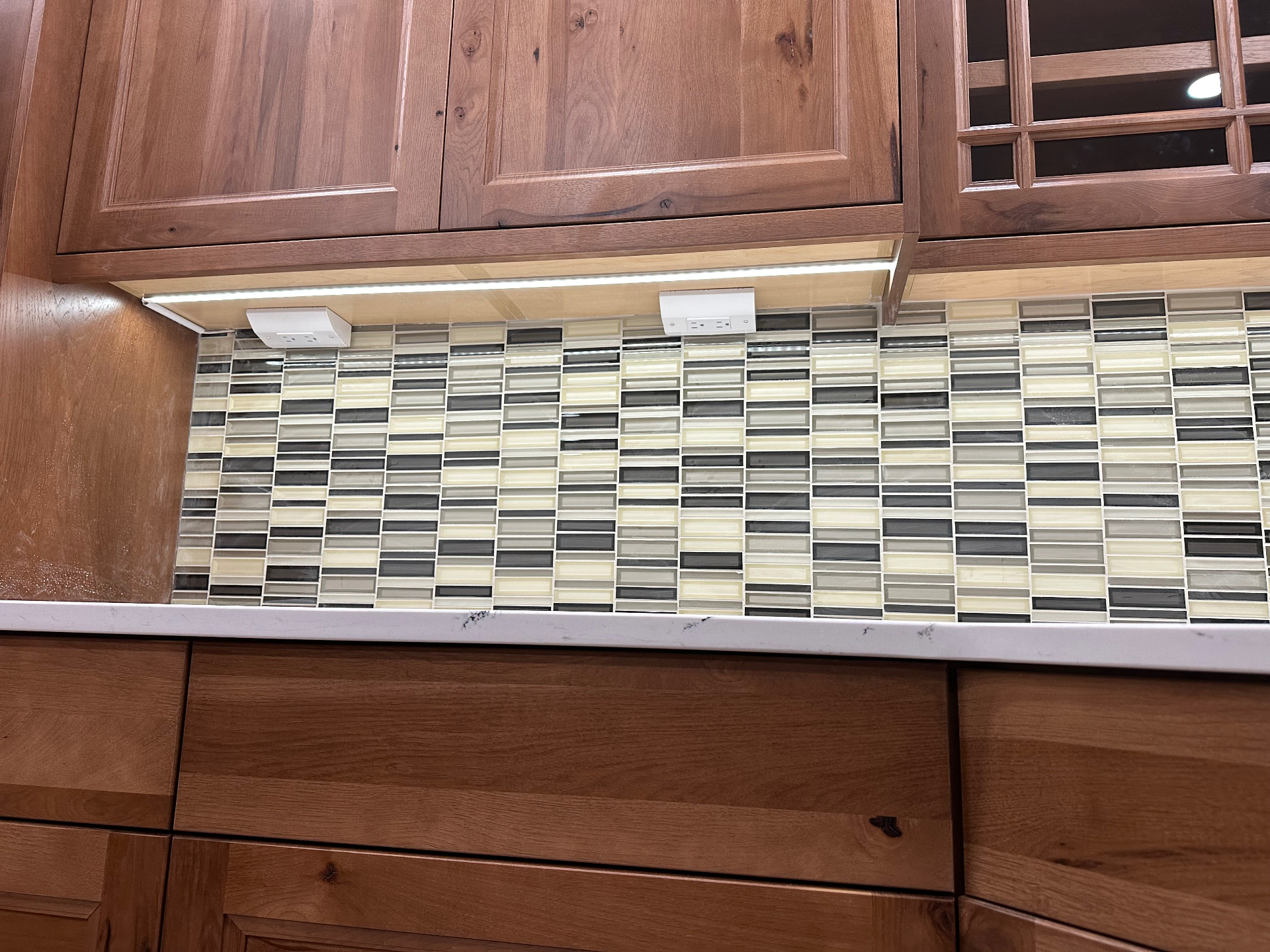 Close detail of LED strip under wood cabinets over mosaic tile backsplash