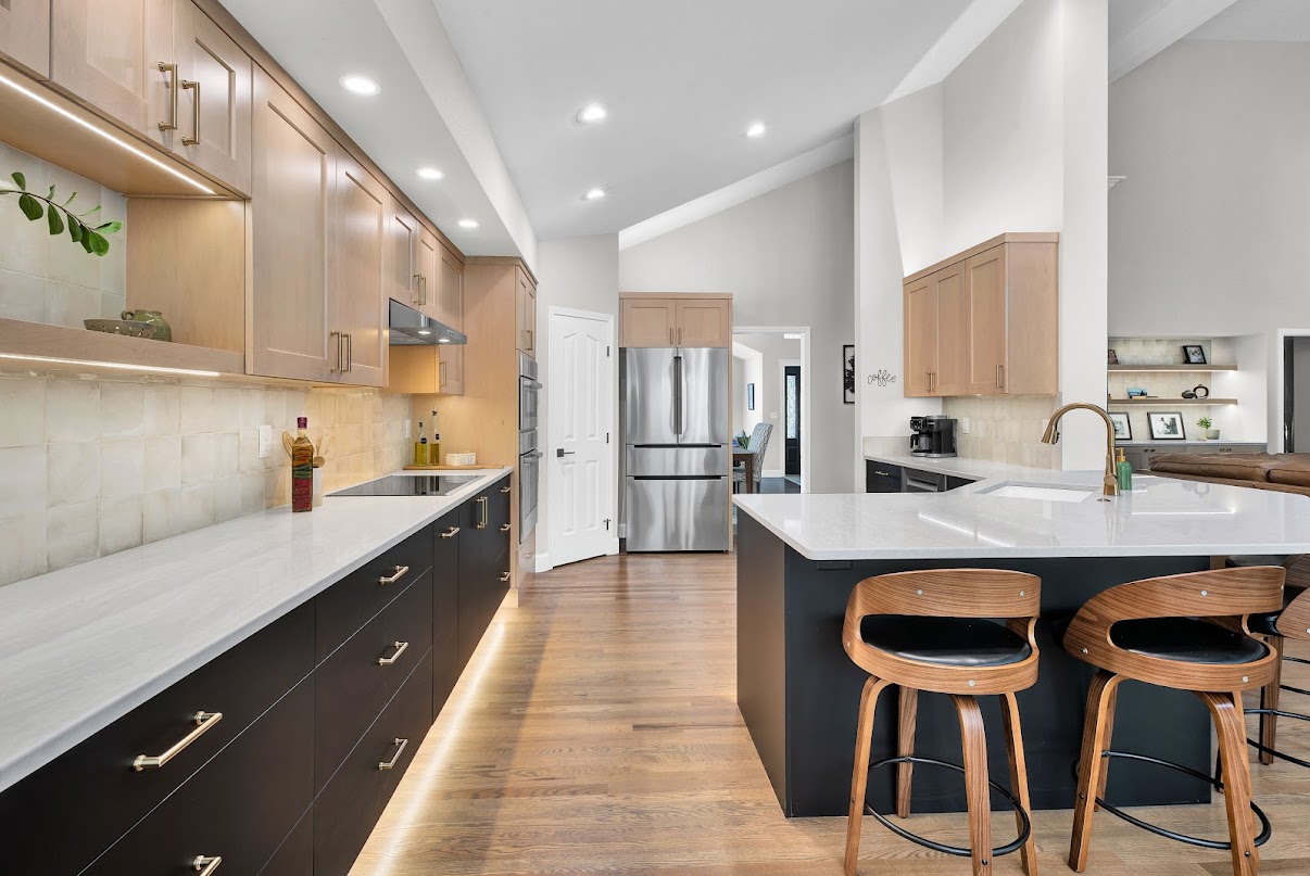 Wide kitchen view with light wood cabinets, dark island, and layered lighting