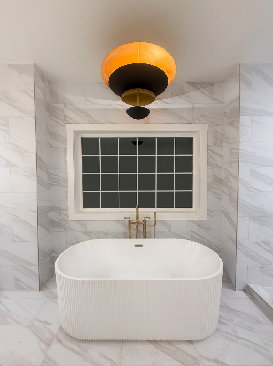 Marble bathroom with freestanding tub and warm sculptural pendant light